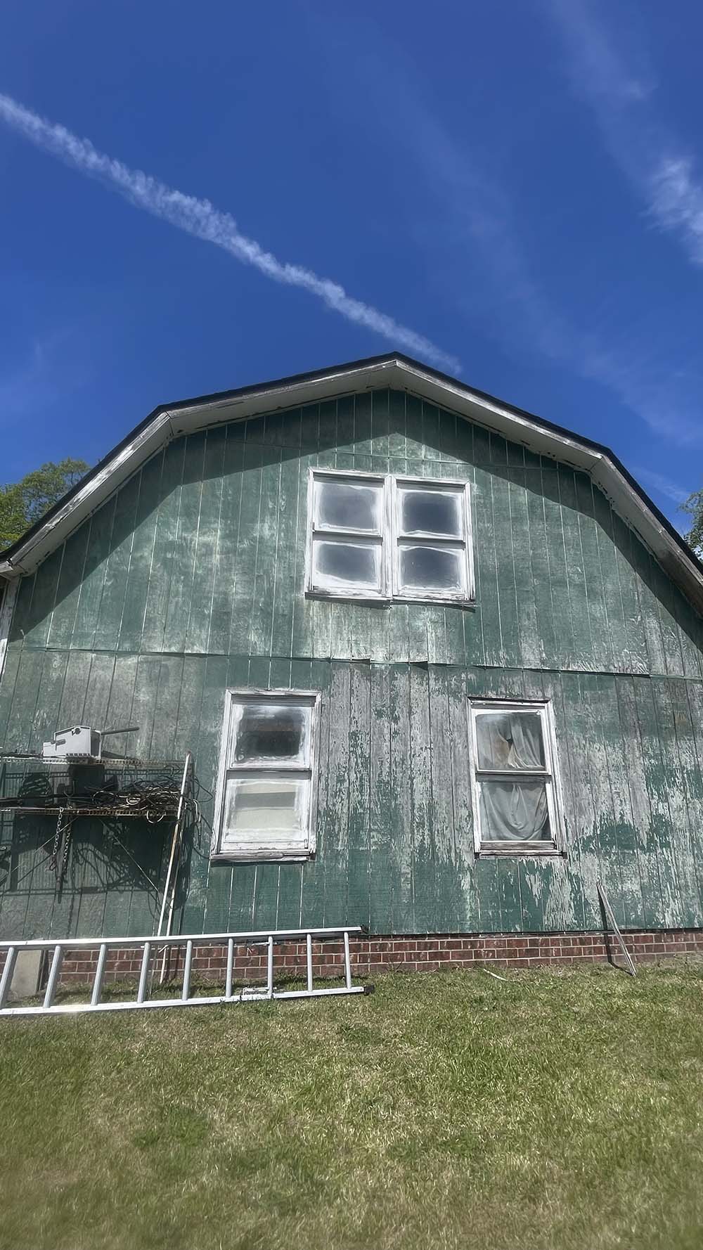 Original weathered green barn siding with curled panels and rotted windows